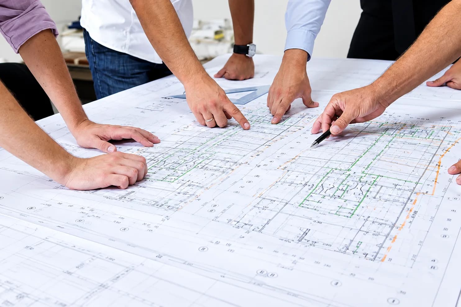 Engineers around a table reviewing a building services drawing, one marking it up with a pen